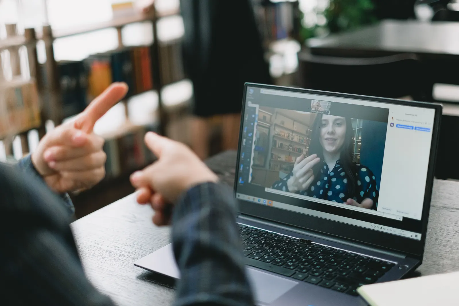 A video call on a laptop, with a woman on screen talking and gesturing.