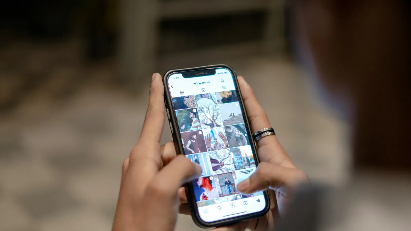 Mãos a segurar um telemóvel com uma grelha de publicações de redes sociais no ecrã.